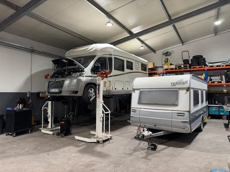 Werkstatthalle von D&W: ein Wohnmobil steht auf der Hebebühne, daneben ein Wohnwagen